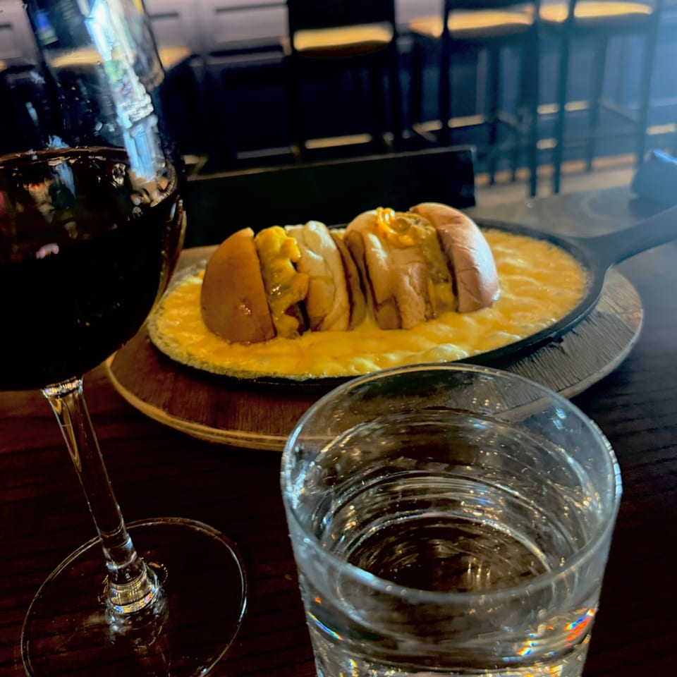 Sliced bread rolls served in creamy sauce on a plate beside a red wine glass and water tumbler.