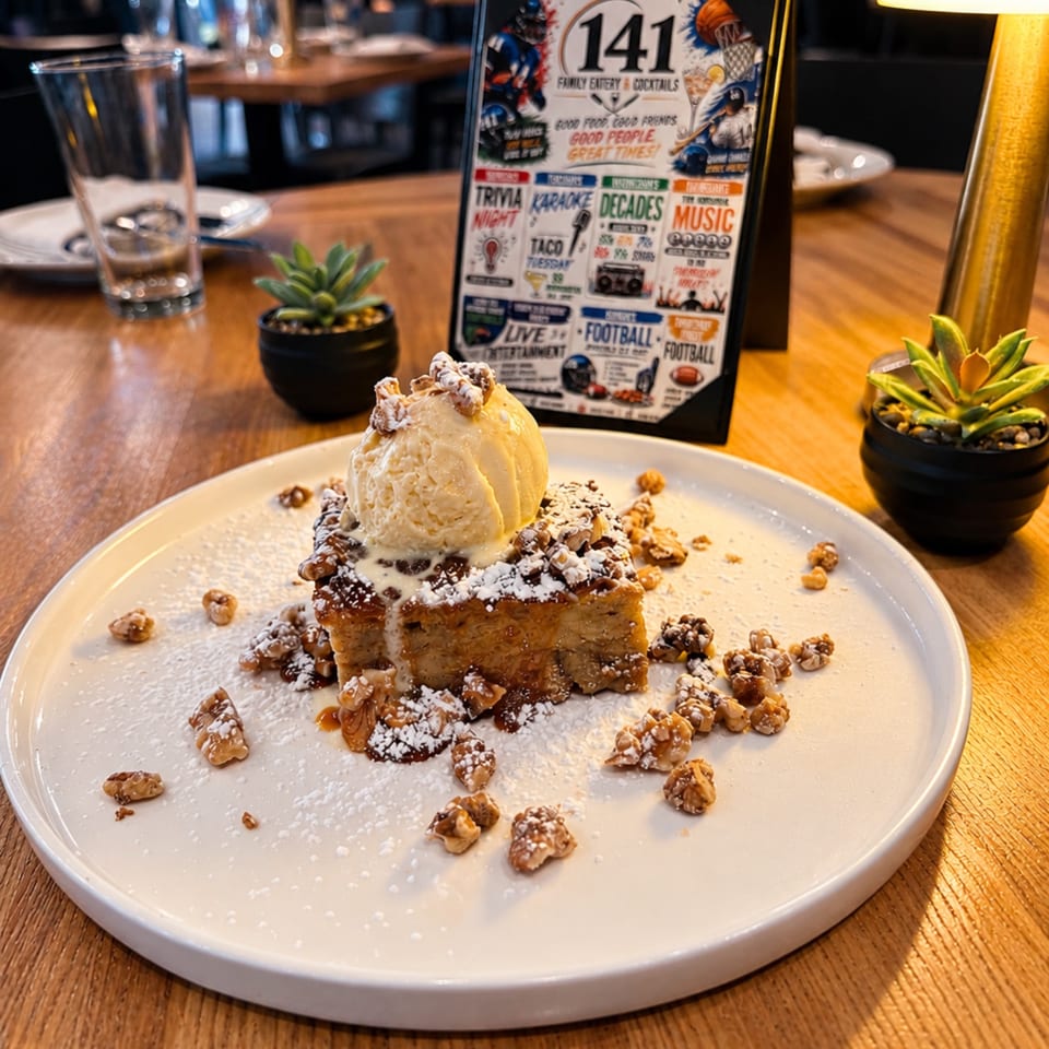 Dessert topped with vanilla ice cream, whipped cream, powdered sugar, chocolate sauce, and chopped nuts on a restaurant table.