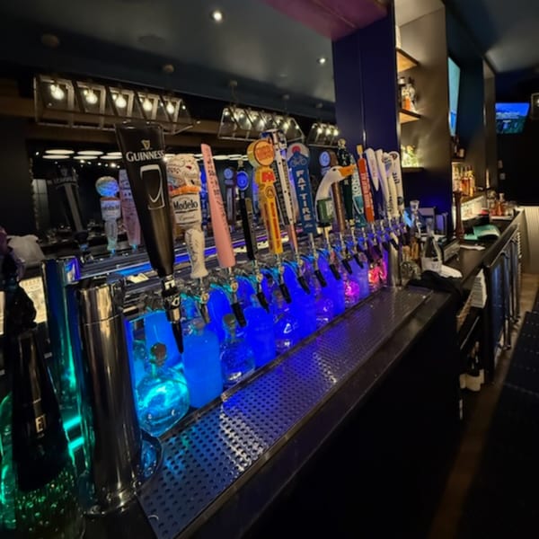 A long bar at Bar 141 with many beer taps illuminated by blue and green lights.