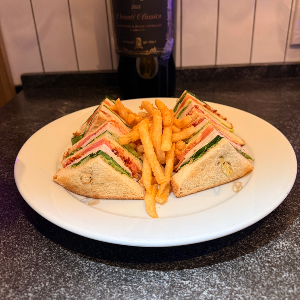 Triangular club sandwiches with layered fillings and crispy fries arranged on a white plate atop a restaurant countertop.