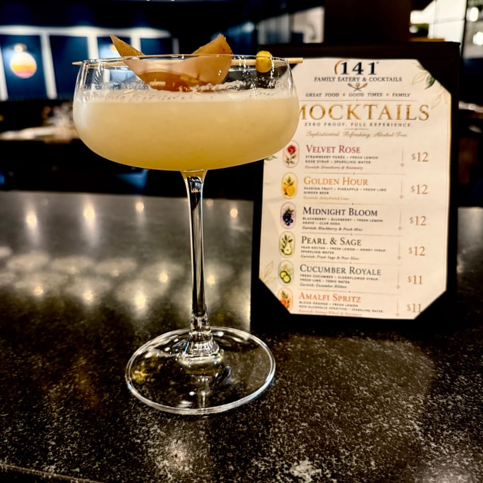 Golden cocktail garnished with citrus peel and a skewer, displayed beside the 141 Family Eatery & Cocktails menu.