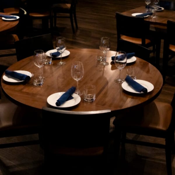 A round wooden table set with white plates, blue napkins, and wine glasses at Bar 141.